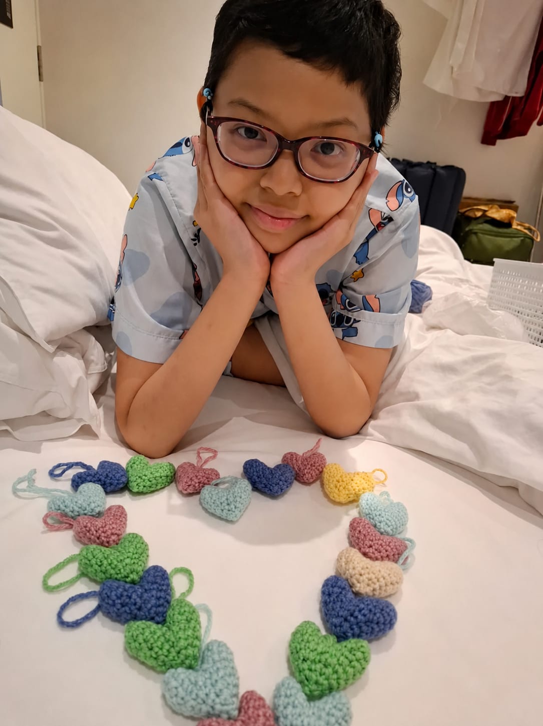 Graceline, a young patient, resting on a hospital bed beside a garland of crocheted hearts